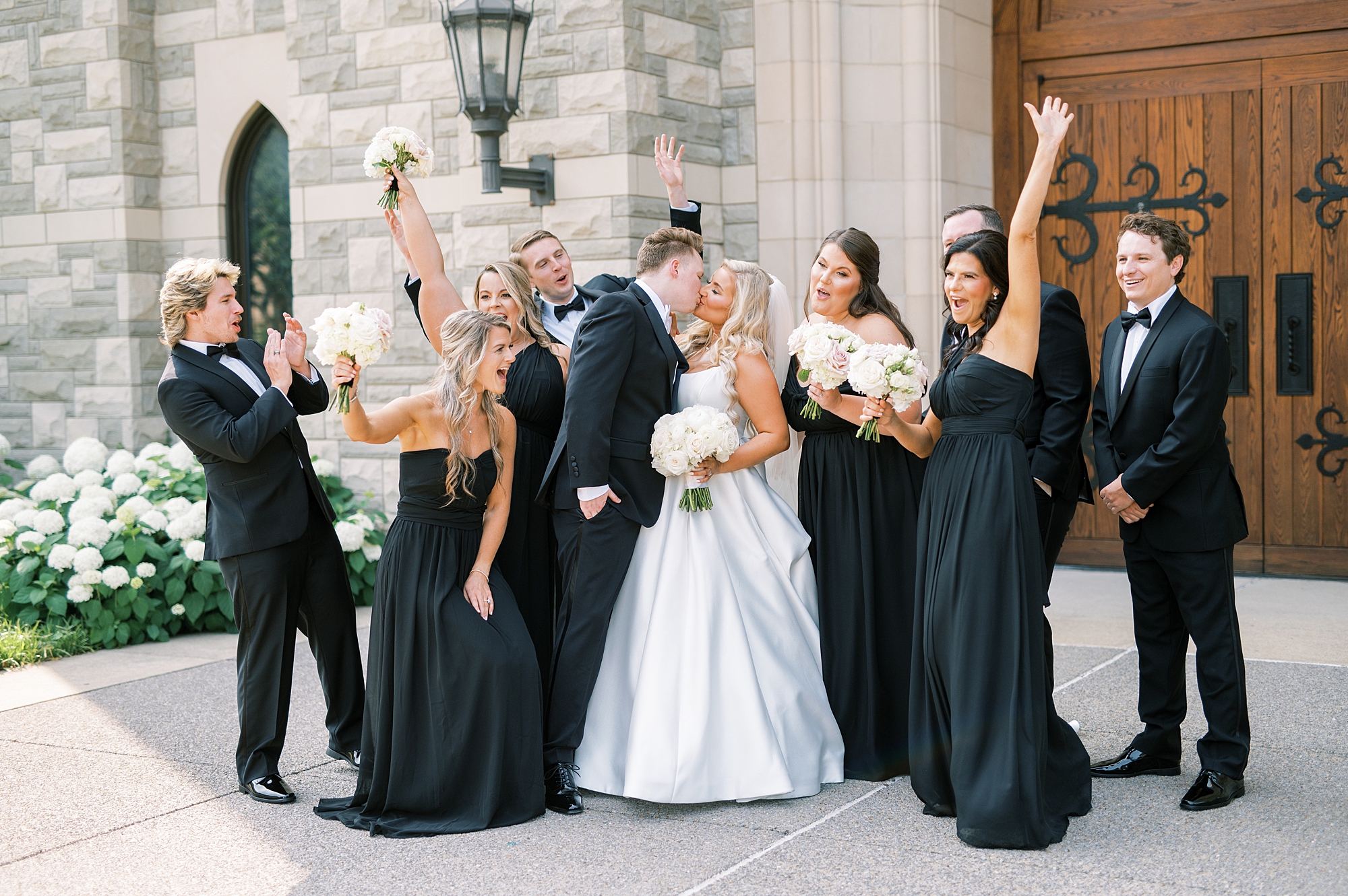 wedding party celebrates as bride and groom kiss 