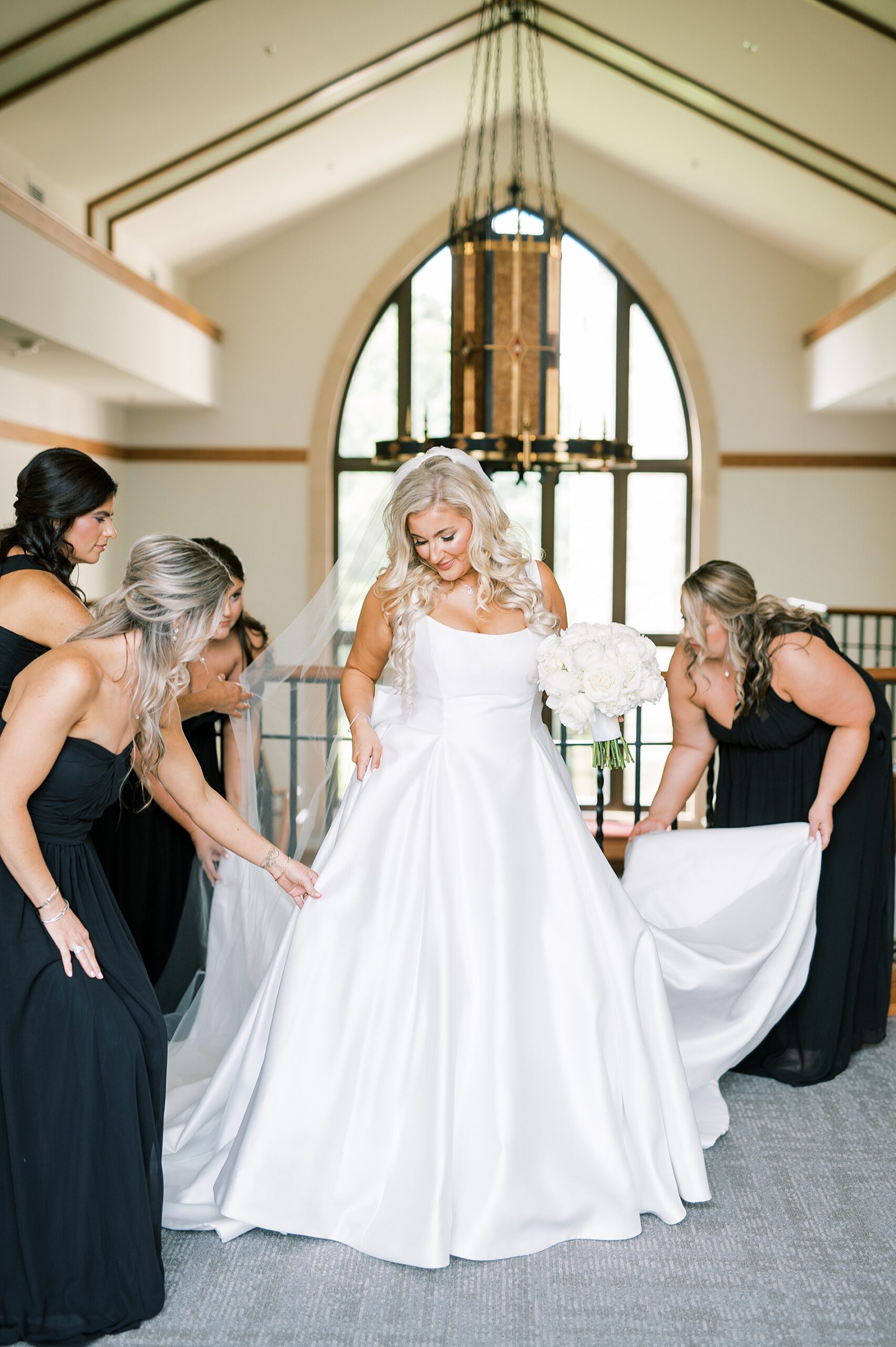 bridesmaids in black dresses helping bride with dress