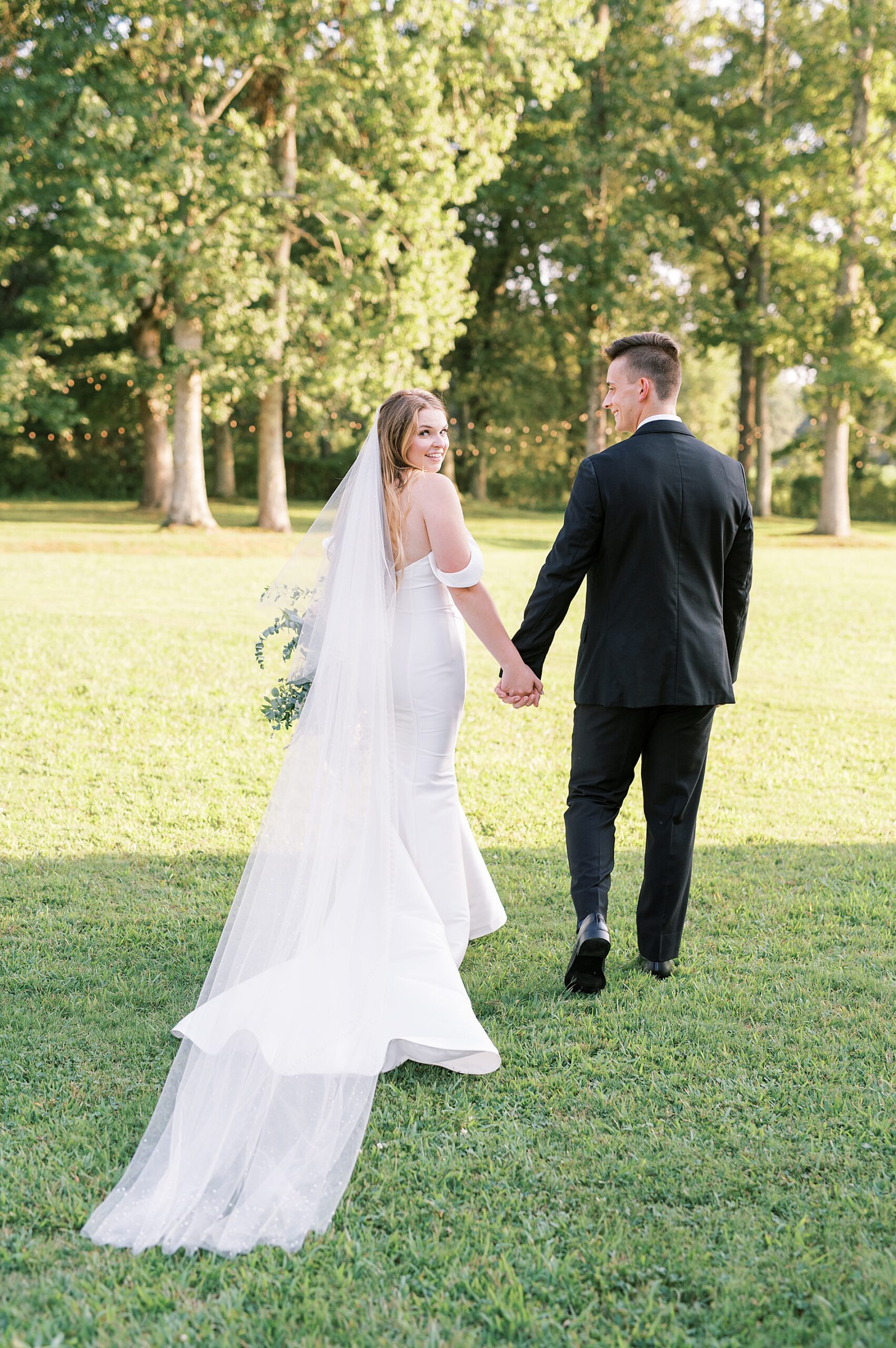 newlyweds hold hands as they walk across the lawn
