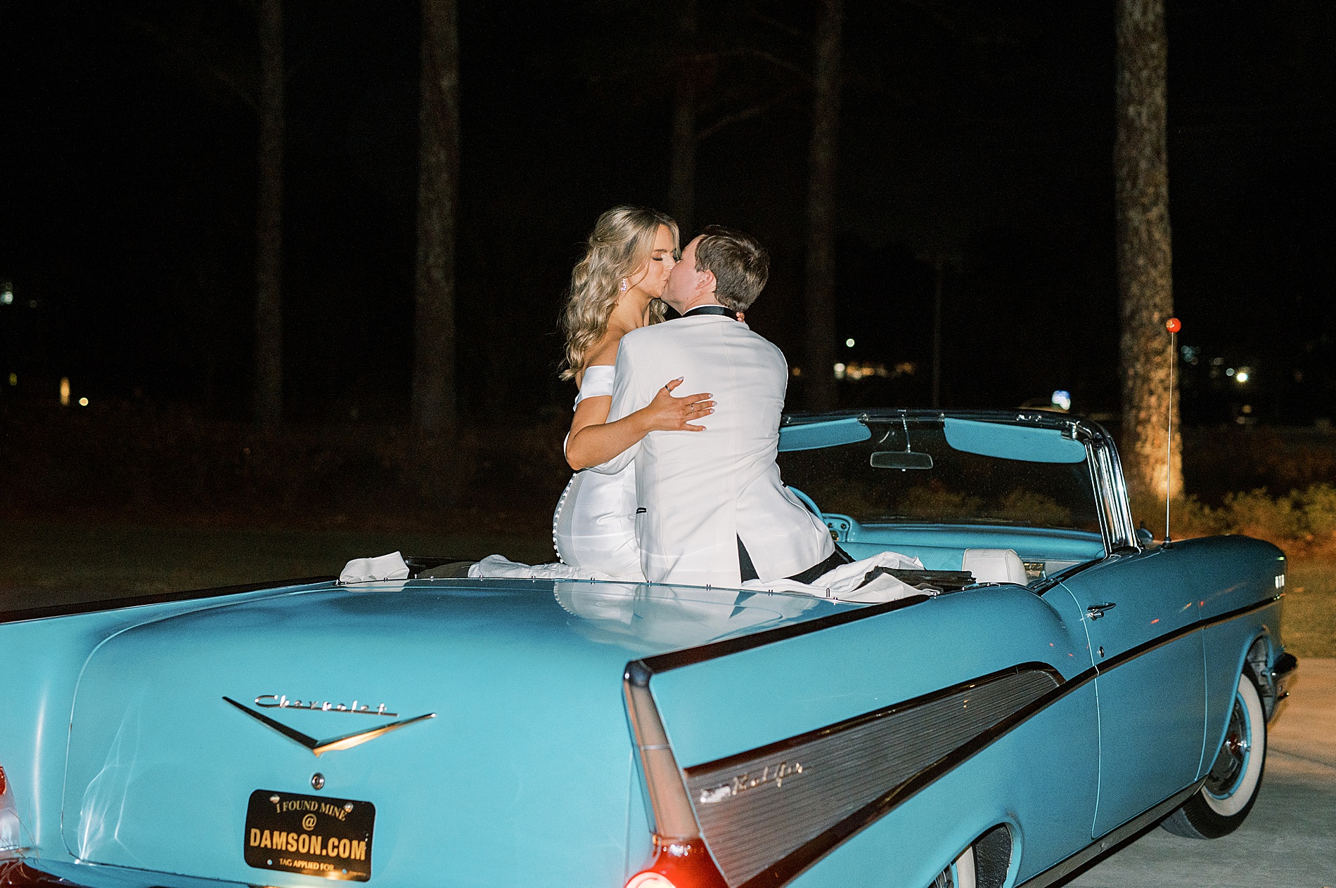 newlyweds kiss sitting on vintage getaway car