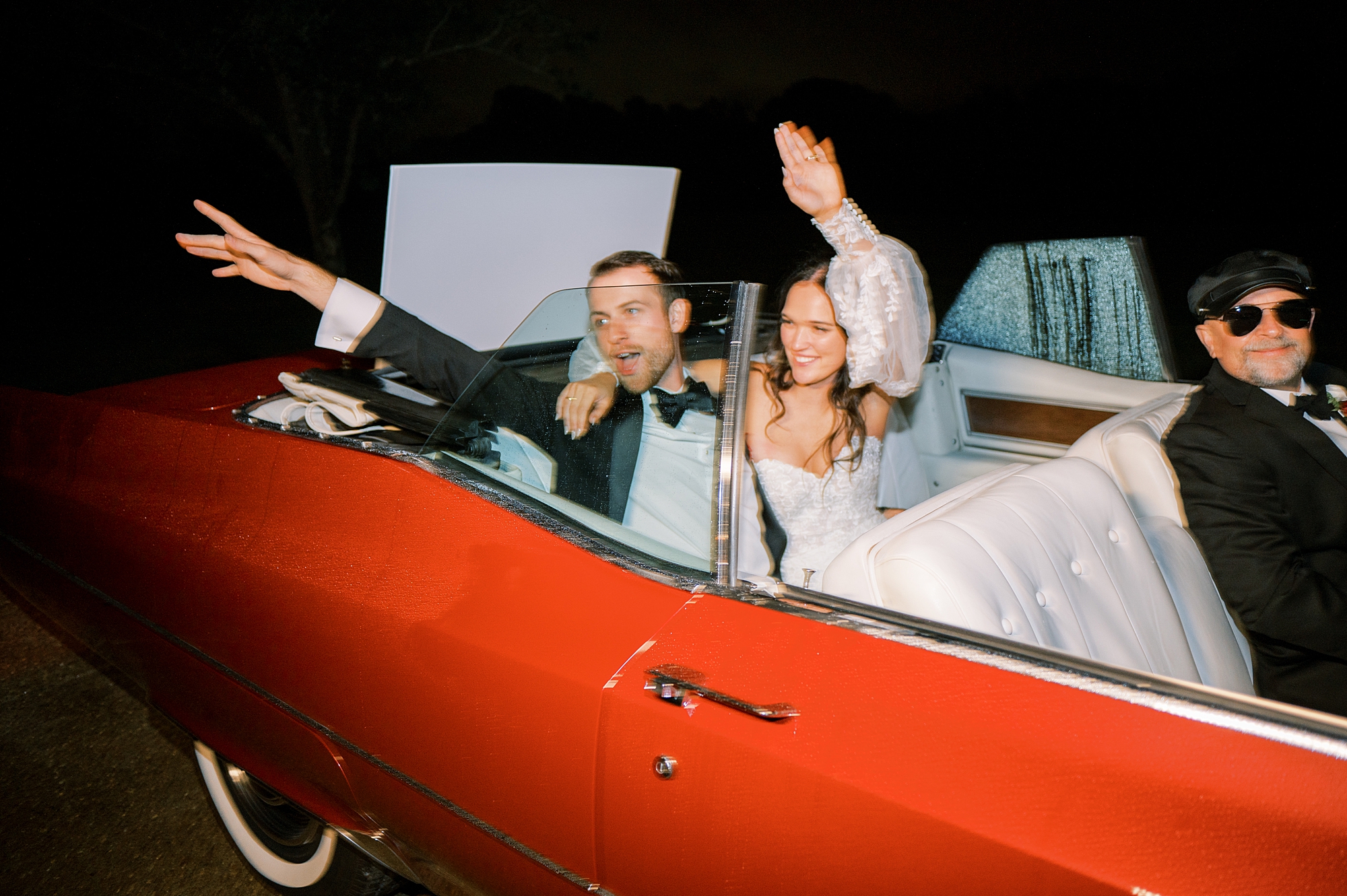 newlyweds wave to their guests as they drive away in red convertible 