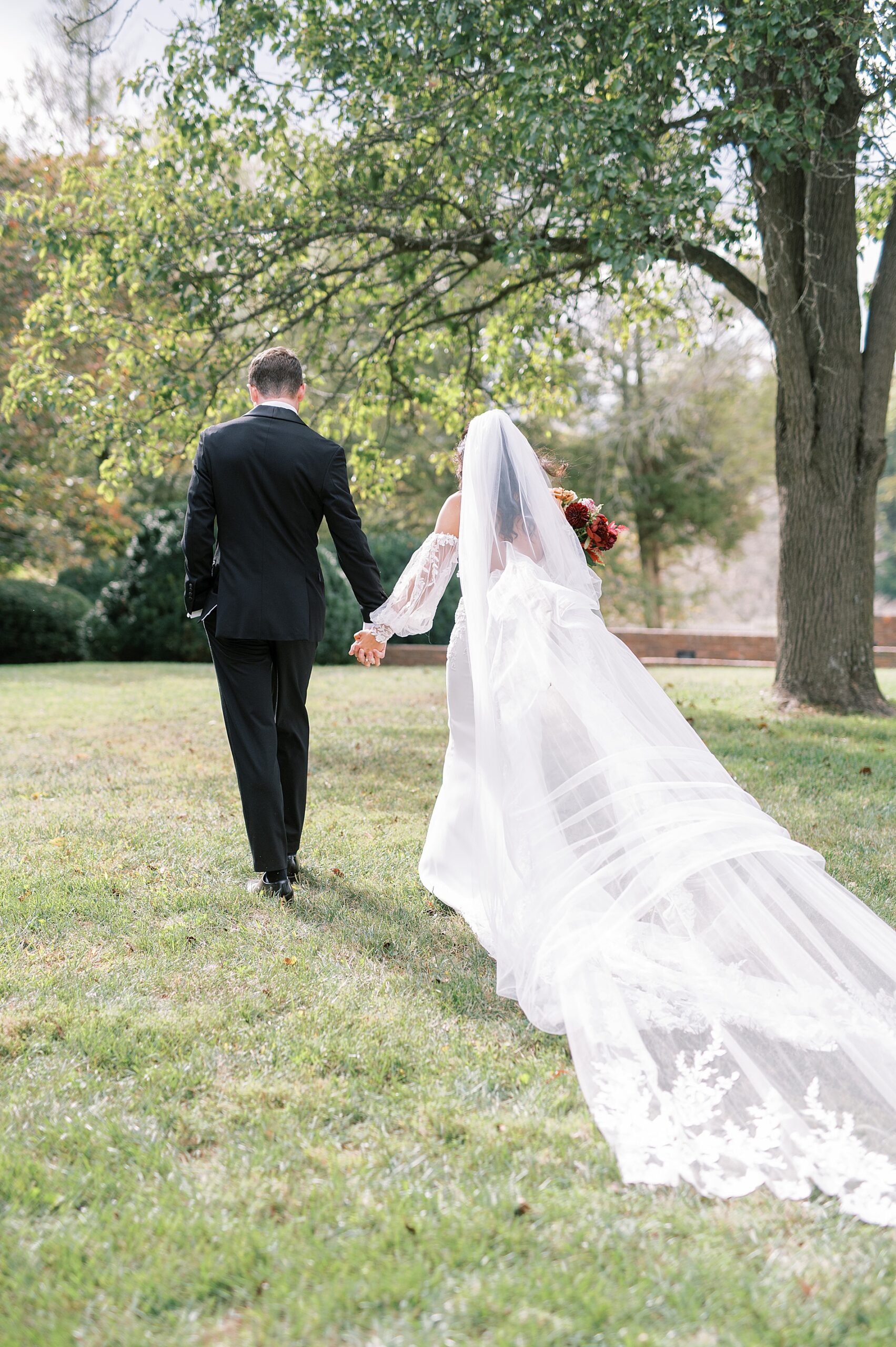 bride and groom hold hands as they walk across  Cedarmont Farm
