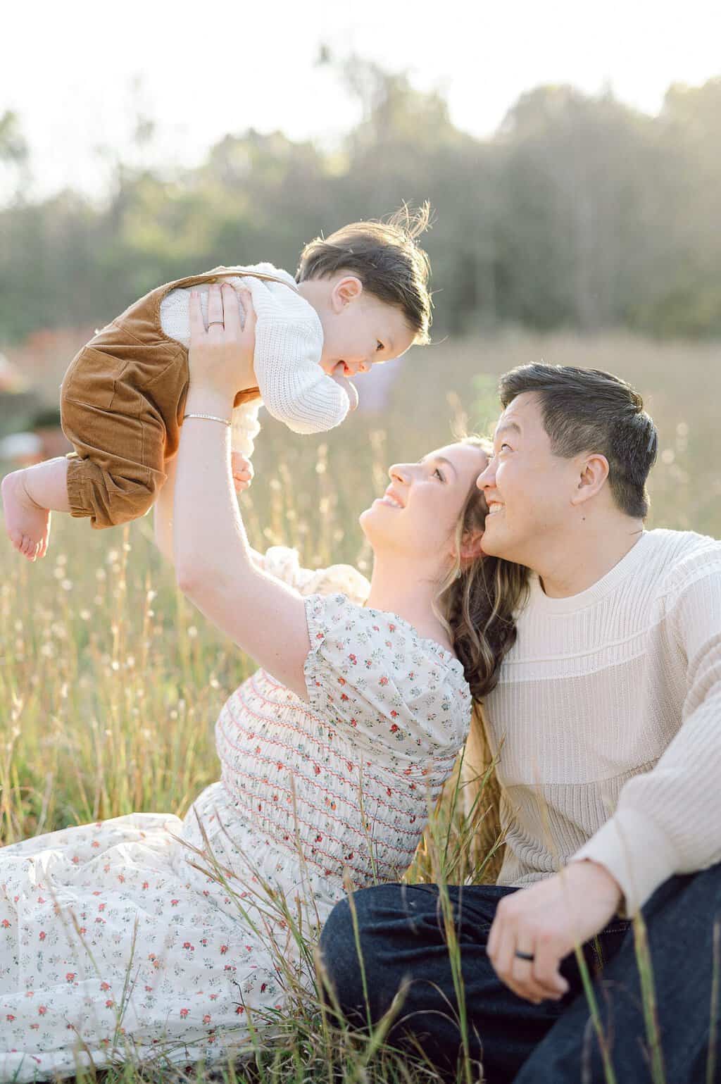 family sits in tall grass with son during golden hour